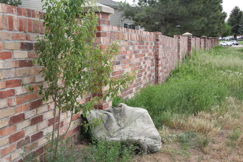 What appears to be a comforter or other bedding lies against a brick wall at the back side of a neighborhood near East Dry Creek Road and South Colorado Boulevard on June 21 in Centennial. City council is considering a ban on camping in certain areas after camping activity was reported in multiple parts of town.